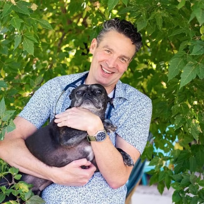 Dr. Benjamin Mackin, owner and veterinarian at Carbondale Animal Hospital, smiling while holding a senior pug 